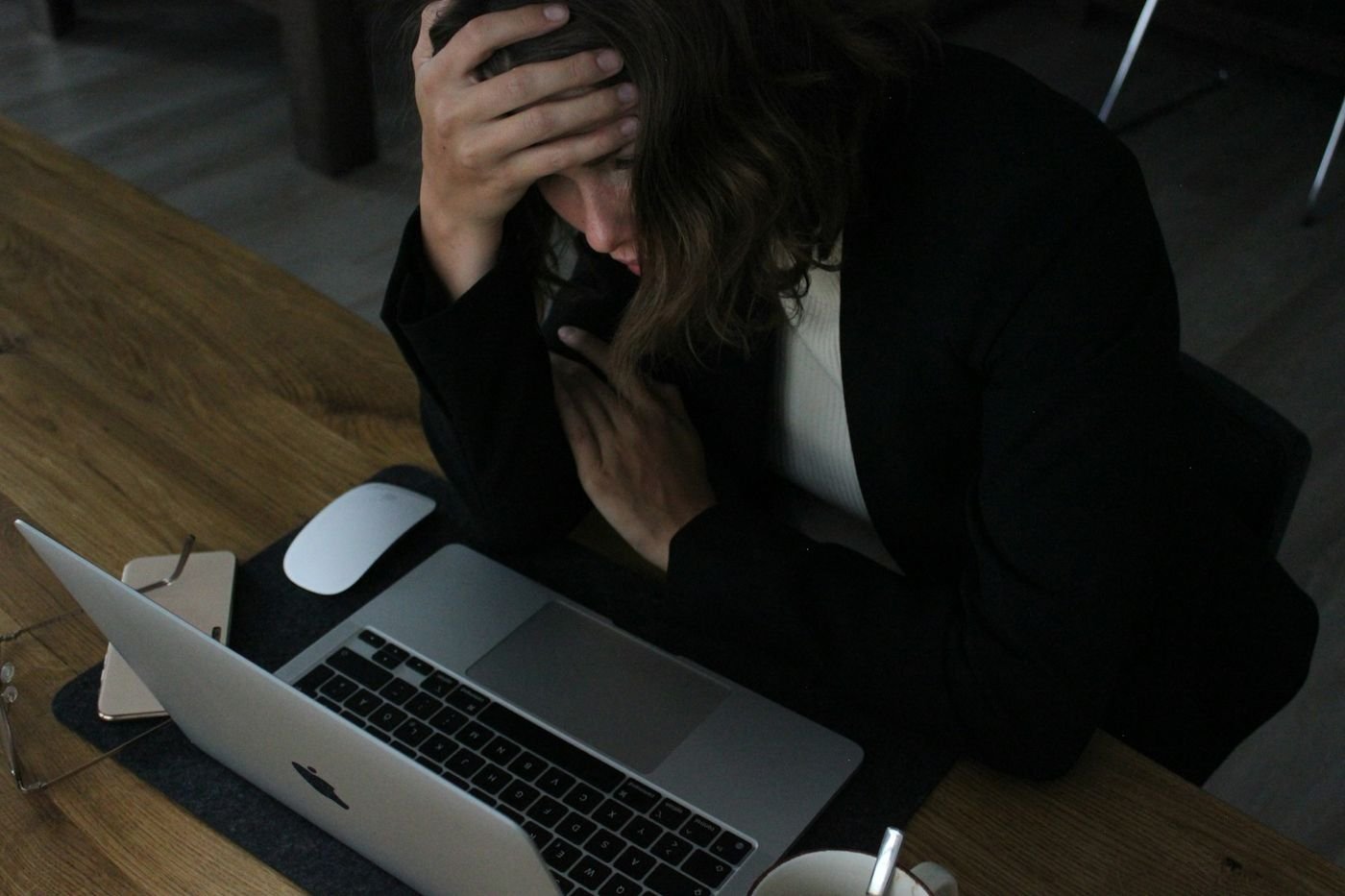 A woman at her desk with her head in her hand, looking at a laptop