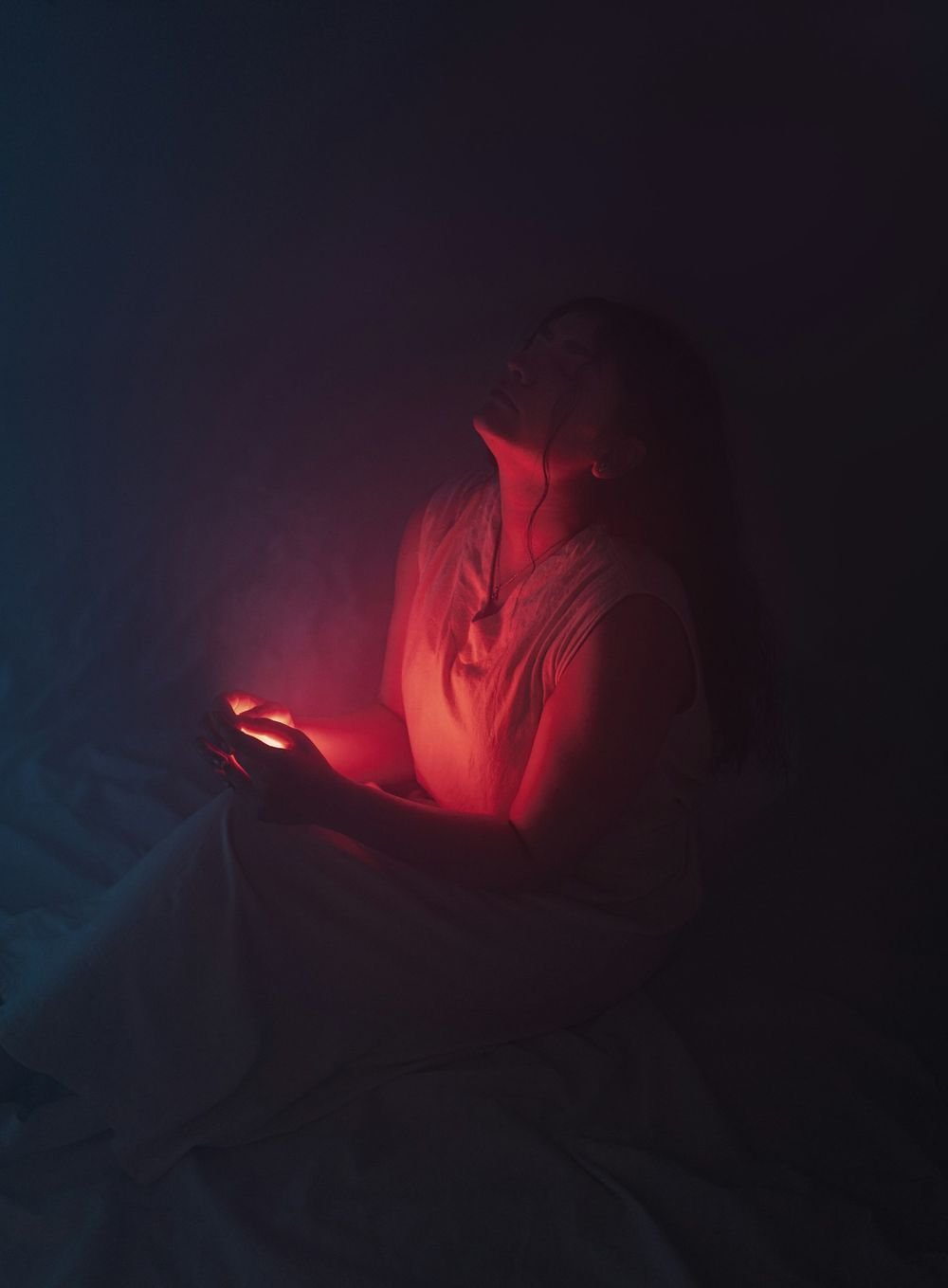 A woman sitting up in bed in the dark, lit by her phone screen
